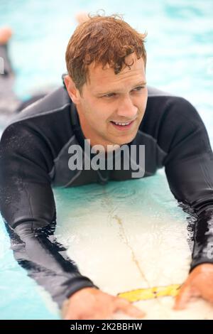 Warten auf die perfekte Welle. Aufnahme eines hübschen jungen Mannes, der in klarem, blauem Wasser surfen kann. Stockfoto