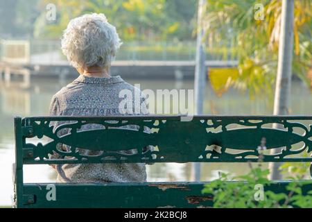 Asiatische ältere Frau deprimiert und traurig sitzen zurück auf Bank im Herbst Park. Stockfoto