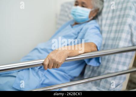 Asiatische ältere oder ältere alte Frau Patient trägt Maske zum Schutz Coronavirus legen Sie sich Griff das Schienenbett mit Hoffnung auf ein Bett im Krankenhaus Stockfoto