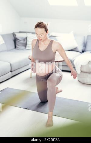 Junge schöne Schwangerin, die zu Hause in ihrem Wohnzimmer Pilates trainiert. Gesunder Lebensstil und aktives Konzept für Schwangerschaft und Mutterschaft. Stockfoto