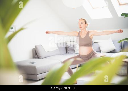 Junge schöne Schwangerin, die zu Hause in ihrem Wohnzimmer Pilates trainiert. Gesunder Lebensstil und aktives Konzept für Schwangerschaft und Mutterschaft. Stockfoto