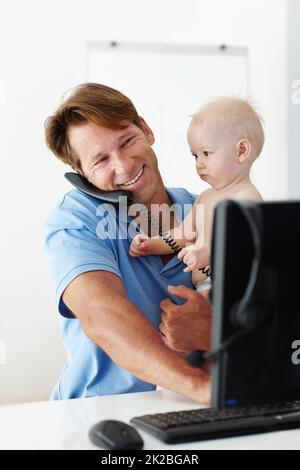 Ich habe eine wichtige Nachricht für Euch Vater erhalten. Aufnahme eines Vaters an seinem Schreibtisch, der ein kleines Kind beim Telefonieren in die Hand nahm. Stockfoto