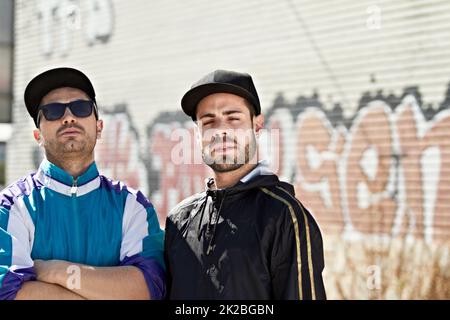 Das Leben auf der Straße. Zwei ernsthafte Männer stehen vor einer Graffiti-Wand. Stockfoto