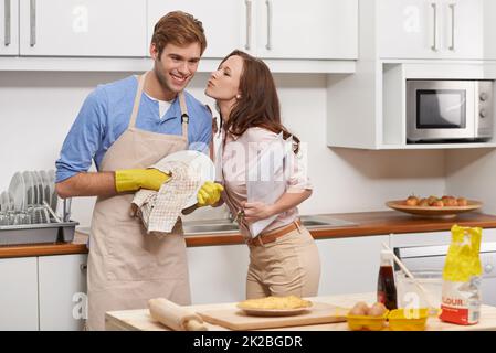 Der perfekte Mann Eine junge Frau küsst ihren Freund Auf Wiedersehen, während sie in der Küche Geschirr trocknet. Stockfoto