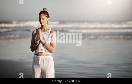 Überlegen Sie sich, wo Sie Ihre Yoga-Routine ruhiger machen können. Kurzer Screenshot einer attraktiven jungen Frau, die am Strand Yoga praktiziert. Stockfoto