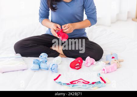 Mutter bereitet Babykleidung vor, die sich auf dem Bett ausruhen und entspannen Stockfoto