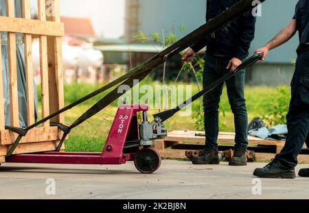 Arbeiter, der mit Handgabelhubwagen zur Liefermaschine in Holzkiste zum Fabriklager arbeitet. Güterverkehr. Schwerlastverkehr. Lager- und Versandgeschäft. Entladen vom Lkw Stockfoto