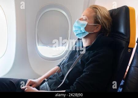 Eine junge Frau mit Gesichtsmaske reist im Flugzeug, Neue normale Reise nach covid-19 Pandemie-Konzept. Stockfoto