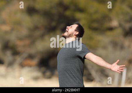 Aufgeregter Mann, der in der Natur schreit und Arme ausstreckt Stockfoto