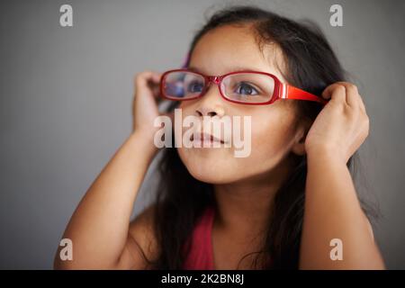 Ich glaube, sie passen zu mir, nicht Sie. Aufnahme eines niedlichen kleinen Mädchens, das eine Brille für Erwachsene anprobiert. Stockfoto