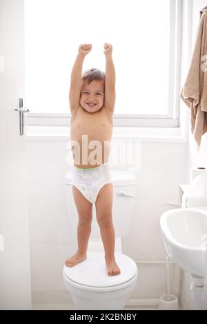 Ich bin jetzt ein großes Kind. Aufnahme eines glücklichen Jungen in einer Windel, der auf einem Toilettensitz steht. Stockfoto