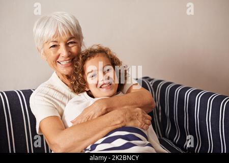 Ich liebe diesen Jungen zu Bits. Aufnahme einer Großmutter, die ihren Enkel umarmt, während sie auf dem Sofa sitzt. Stockfoto