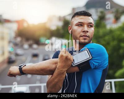 Machen Sie sich bereit für etwas Action. Aufnahme eines jungen Mannes, der sich vor einem Lauf in der Stadt ausdehnt. Stockfoto