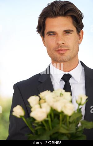 Ein Friedensangebot. Porträt eines hübschen jungen Mannes, der einen Anzug trägt und einen Strauß Rosen in der Hand hält. Stockfoto