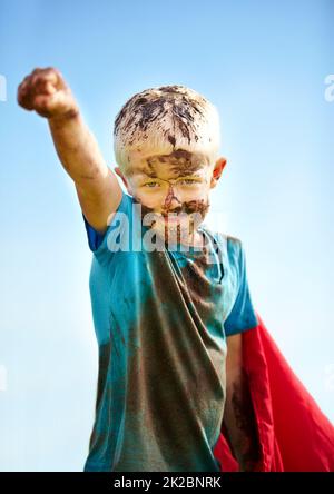 Ein schlammiger Superheld. Ein kleiner Junge, der als Superheld verkleidet und mit Schlamm bedeckt ist. Stockfoto