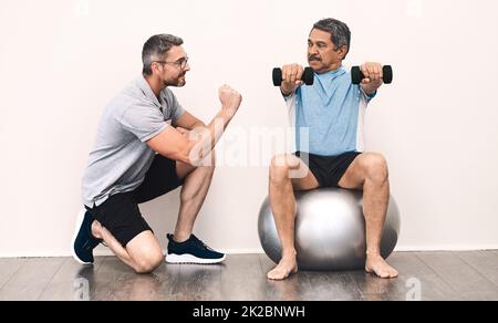 Gleichgewicht ist der Schlüssel zu allem im Leben. Ganzkörperaufnahme eines Seniorenmannes, der während einer Rehabilitationssitzung mit seinem Physiotherapeuten mit Kurzhanteln trainiert. Stockfoto