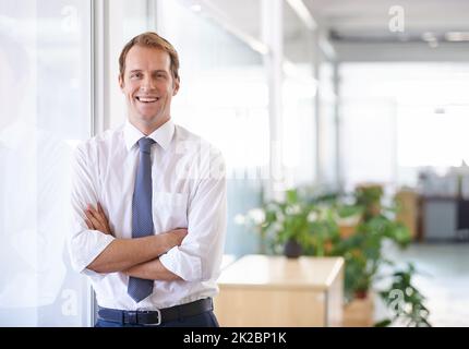 Erfolg ist nicht zufällig. Porträt eines hübschen Geschäftsmanns, der sich an einer Glaswand lehnt. Stockfoto