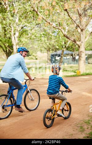 Frische Luft und Bewegung mit den Jungs. Aufnahme eines Vaters und seines kleinen Sohnes, der durch einen Park Fahrrad fährt. Stockfoto