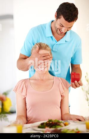 Überraschung. Ein gutaussehender Mann bedeckt seine Freundinnen von hinten, während er ihr eine Ringbox reicht. Stockfoto