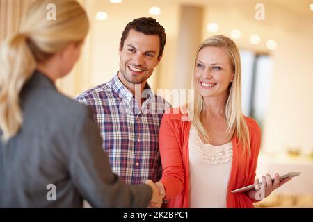 Finanzielle Beratung, der Sie vertrauen können. Ein glückliches Paar schüttelt sich die Hände mit ihrem Finanzberater bei sich zu Hause. Stockfoto