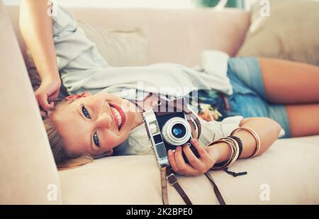 Lassen Sie Ihre Worte wenige und Ihre Enthüllungen viele sein. Porträt einer schönen jungen Frau, die ihre Kamera hält, während sie auf einer Couch liegt. Stockfoto