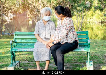 Pflegepersonal helfen und sprechen mit asiatischen älteren oder älteren alten Dame Frau trägt eine Gesichtsmaske zum Schutz der Sicherheitsinfektion Covid19 Coronavirus im Park. Stockfoto