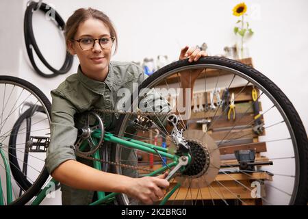 Mädchen können auch Dinge reparieren. Aufnahme einer jungen Frau, die während der Befestigung eines Fahrrads auf die Kamera schaut. Stockfoto