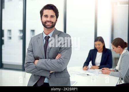 HES führt den Weg nach vorn. Porträt eines Geschäftsmannes, der in einem Sitzungssaal mit Kollegen im Hintergrund steht. Stockfoto