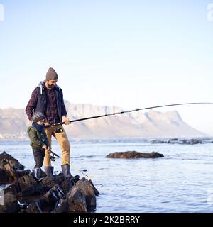 Es sieht so aus, als ob du etwas hast. Aufnahme eines niedlichen kleinen Jungen, der mit seinem Vater am Meer fischt. Stockfoto