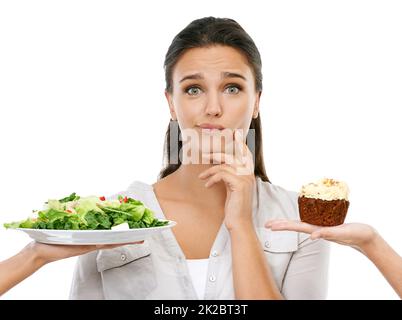 Sollte ich oder nicht. Studioaufnahme einer jungen Frau, die sich zwischen einer gesunden und ungesunden Ernährung entscheidet. Stockfoto