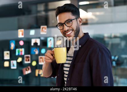 Es gibt nichts, was man mit einer guten Tasse Kaffee nicht reparieren kann. Verkürztes Porträt eines gutaussehenden jungen Geschäftsmannes, der eine Brille trägt und in seinem Büro steht, während er eine Tasse Kaffee trinkt. Stockfoto