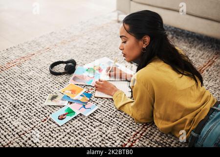 Ich muss das beste Bild aussuchen. Gekürzte Aufnahme einer attraktiven jungen Geschäftsfrau, die auf ihrem Wohnzimmerboden liegt und Polaroide für ihren Blog sortiert. Stockfoto