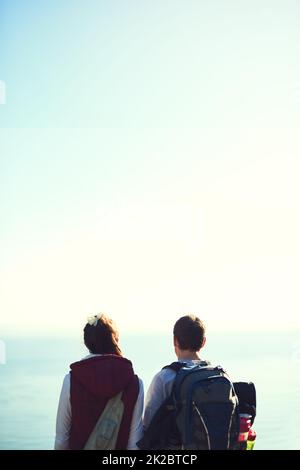 Trinken in der Aussicht. Rückansicht eines jungen Paares, das die Aussicht von der Spitze eines Berges bewundert. Stockfoto