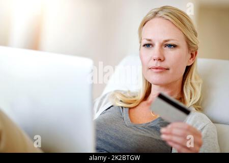 Klicken Sie auf „Klicken“, um zu kaufen. Aufnahme einer Frau, die zu Hause auf ihrem Sofa online einkaufen geht. Stockfoto