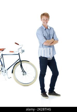 Mit Stil herumkommen. Ein hübscher junger rotköpfiger Mann, der neben einem altmodischen Fahrrad mit gefalteten Armen steht. Stockfoto