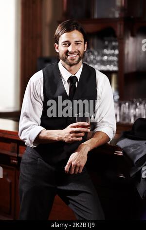 Entspannen bei einem Drink. Porträt eines gut gekleideten jungen Mannes, der bei einem Drink an einer Bar steht. Stockfoto