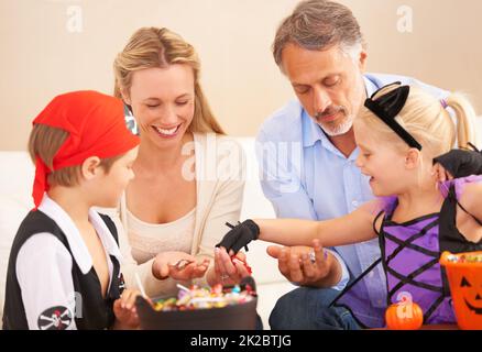 Familie bereit zum Schlemmen. Eine Familie sitzt zusammen und teilt Süßigkeiten an halloween mit Kindern in schickem Kleid. Stockfoto