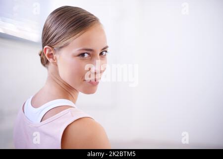 Lass uns fit werden. Eine kurze Aufnahme einer attraktiven jungen Frau im Fitnessstudio, die über ihre Schulter schaut. Stockfoto