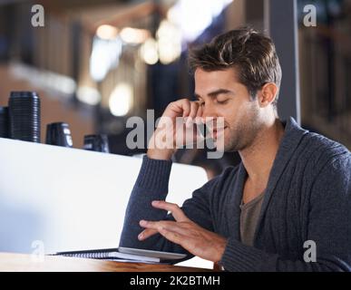 Einen Freund für Kaffee anrufen. Ein junger Mann, der in einem Café sitzt und auf seinem Handy spricht und an einem digitalen Tablet arbeitet. Stockfoto