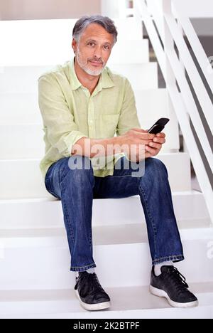 Senden eines Textes aus den Schritten. Ein reifer Geschäftsmann, der sein Mobiltelefon benutzt, während er im Büro sitzt. Stockfoto