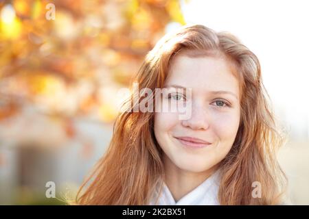 Sie liebt den Look des Herbstes. Porträt eines hübschen jungen Mädchens, das draußen unter den Herbstbäumen steht. Stockfoto