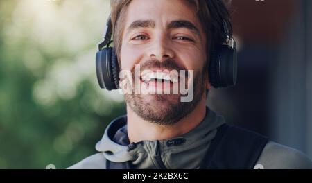 Musik macht meinen Tag. Eine Aufnahme eines jungen Mannes, der Kopfhörer trug, während er durch die Stadt ging. Stockfoto