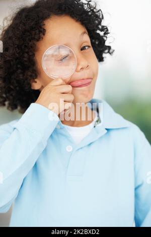 Hes ein neugieriger Geist. Porträt eines niedlichen Jungen, der mit einer Lupe über sein geschlossenes Auge schaut. Stockfoto