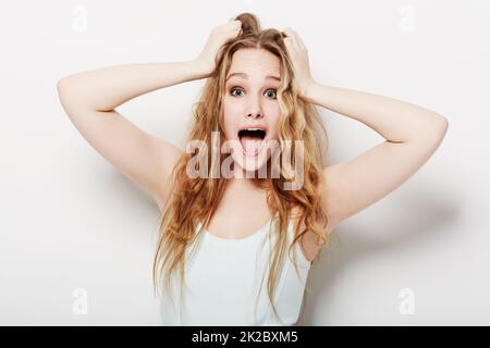 Wow, ich kann es kaum glauben. Überraschte die junge Frau mit ihren Händen im Haar. Stockfoto