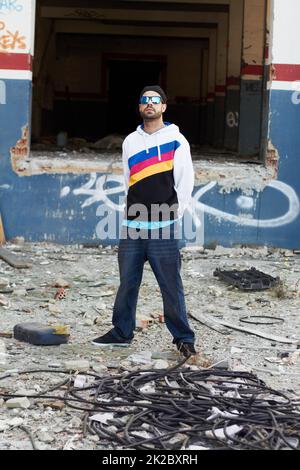 Das urbane Leben. Ein trendiger Mann, der vor einer Graffiti-Wand in einem Schrottplatz steht. Stockfoto