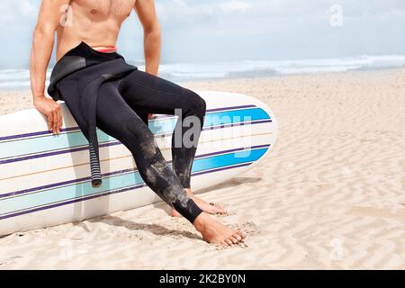 Surfen ist eine Lebensart. Ein junger männlicher Surfer, der sich an einem heißen Sommertag auf eine Brandung vorbereitet. Stockfoto