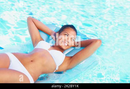 Jetzt ist dies ein Urlaub. Beschnittene Ansicht einer lächelnden jungen Frau, die auf einer Lilo in einem Pool schwimmt. Stockfoto