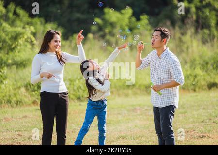 Asiatische Familie Mutter, Vater und kleines Mädchen mit Spaß zusammen spielen Blasen Seifenblasen im Park Stockfoto