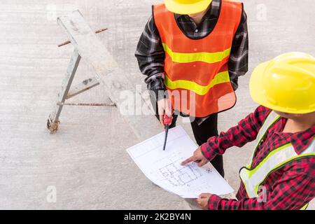 Der Architekt und der Kunde, der mit ihm spricht, helfen bei der Erstellung eines Plans mit dem Bauplan des Gebäudes auf dem Boden der Baustelle. Asiatischer Ingenieur Vorarbeiter, Mann und Frau, Meeting und Planung von Bauarbeiten, Draufsicht Stockfoto