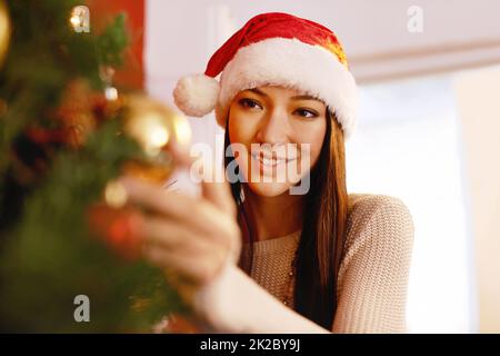 Den Baum hell und glänzend machen. Kurzer Schuss einer attraktiven jungen Frau, die einen Weihnachtsbaum schmückt. Stockfoto